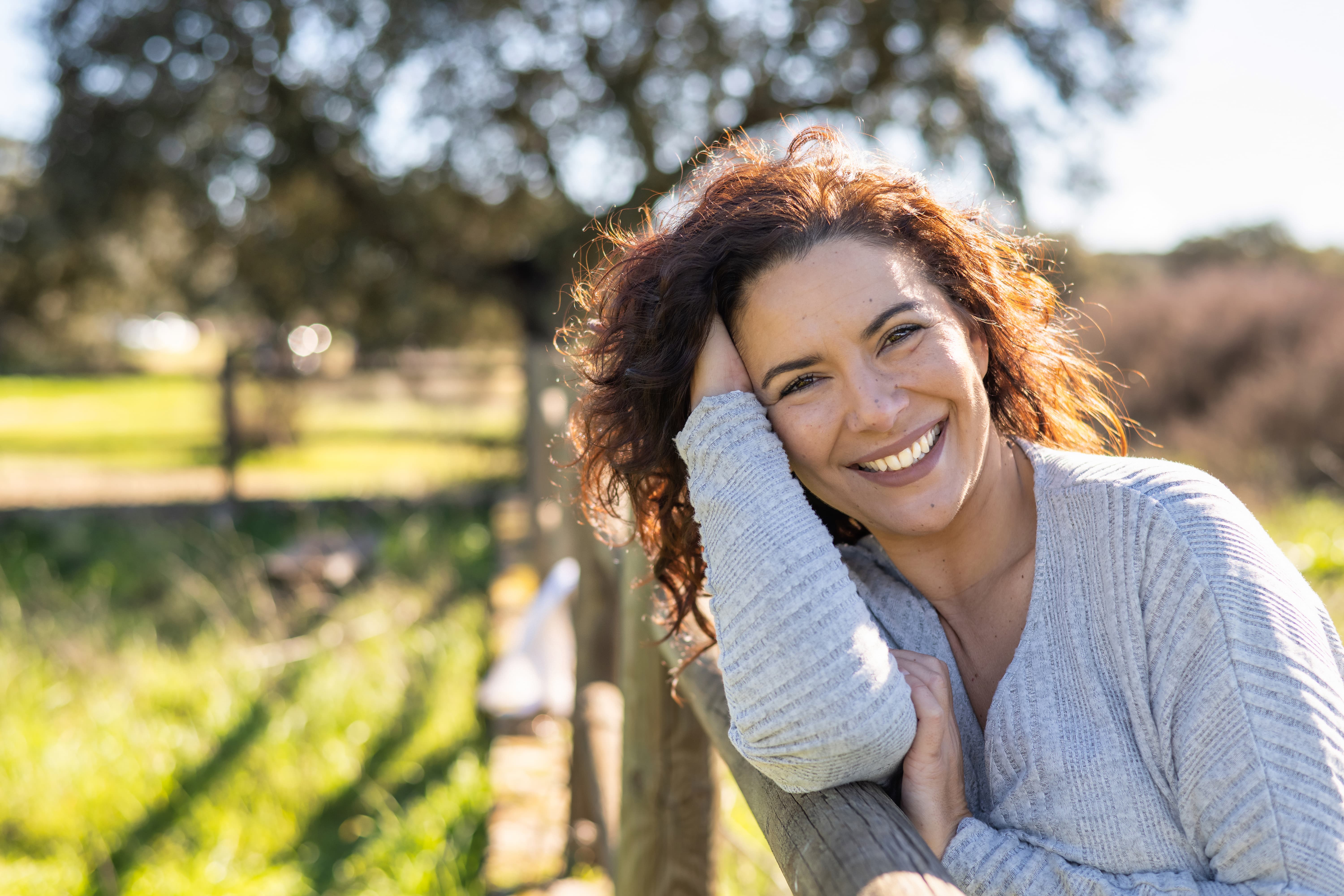 A woman smiling, leaning on a wooden fence in the sun