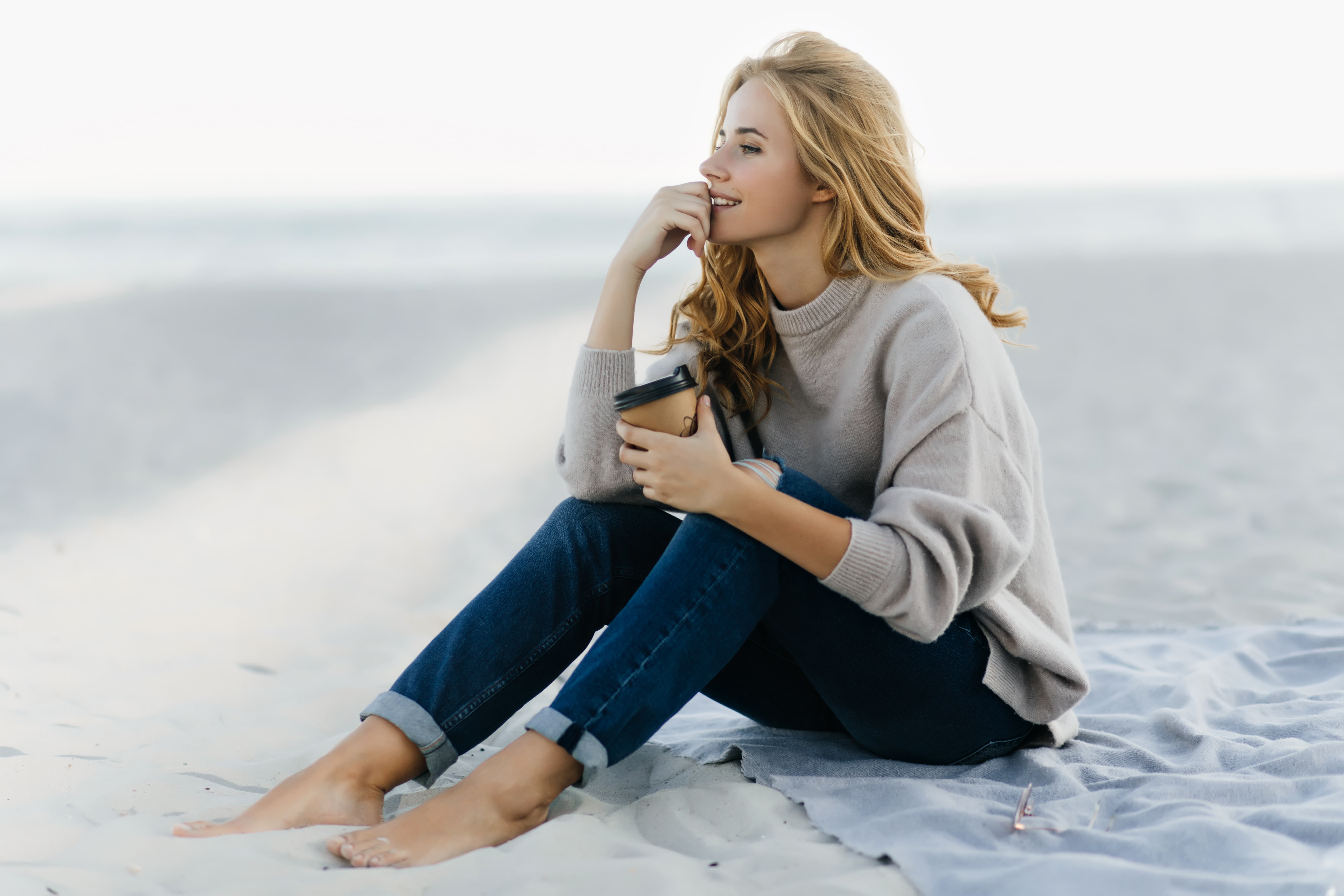 A woman sitting quietly on the sand, looking out at the horizon